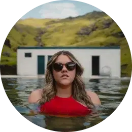 Entspannter Reisender in den malerischen heißen Quellen Islands Frau im roten Badeanzug und mit Sonnenbrille, die ein natürliches Thermalbecken in Island genießt.