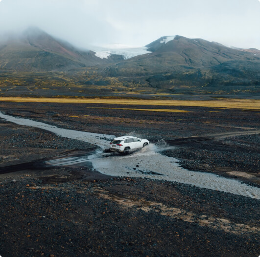 Ein Land Rover Discovery steht in einer rauen isländischen Landschaft mit roter Erde und felsigen Klippen, das abenteuerliche Design des SUVs unter einem strahlend blauen Himmel hervorhebend.
