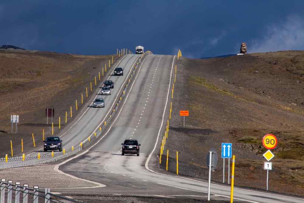 Autos auf Islands Route 1 neben einem Verkehrsschild mit 90-km/h-Geschwindigkeitsbegrenzung in einer abgelegenen Vulkanlandschaft.
